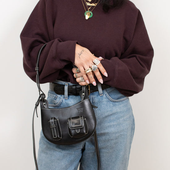 Person wearing a maroon sweater and blue jeans, holding a black handbag against a white background