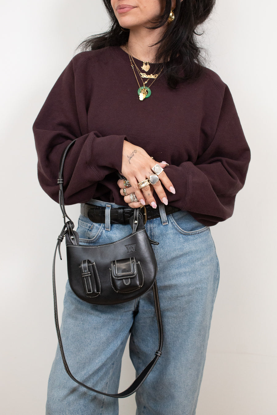 Person wearing a maroon sweater and blue jeans, holding a black handbag against a white background