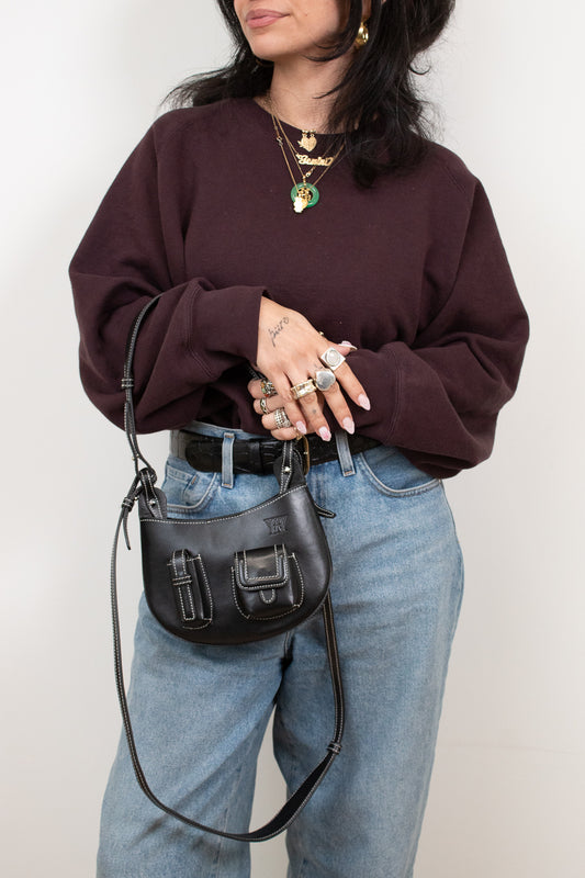 Person wearing a maroon sweater and blue jeans, holding a black handbag against a white background