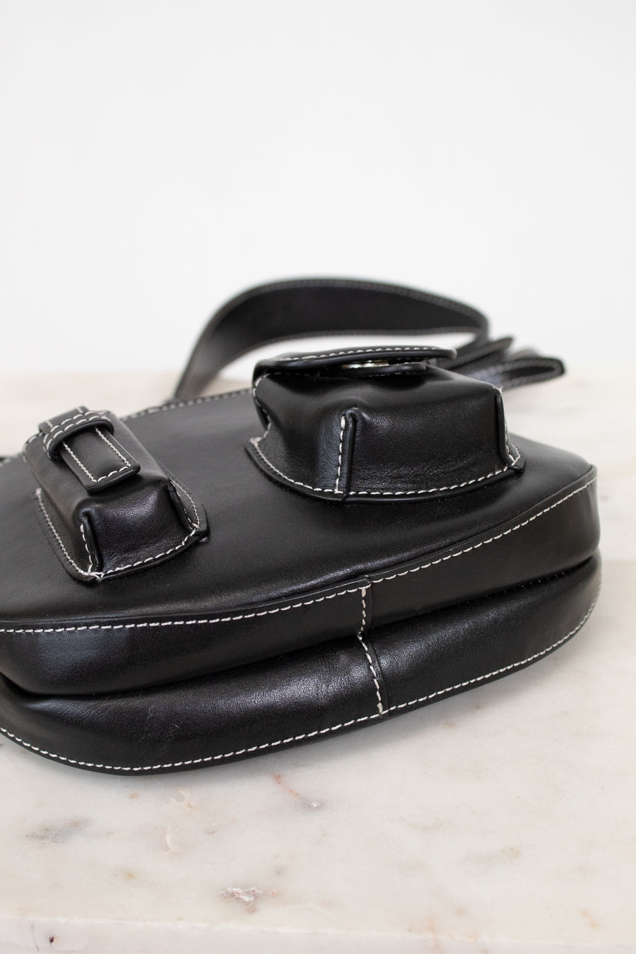 Black leather bag with buckle details on a marble surface