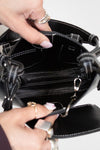 Close-up of a person opening a black handbag with handle.