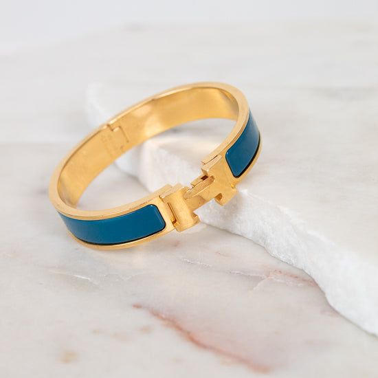 Teal and gold bracelet with H clasp on white background