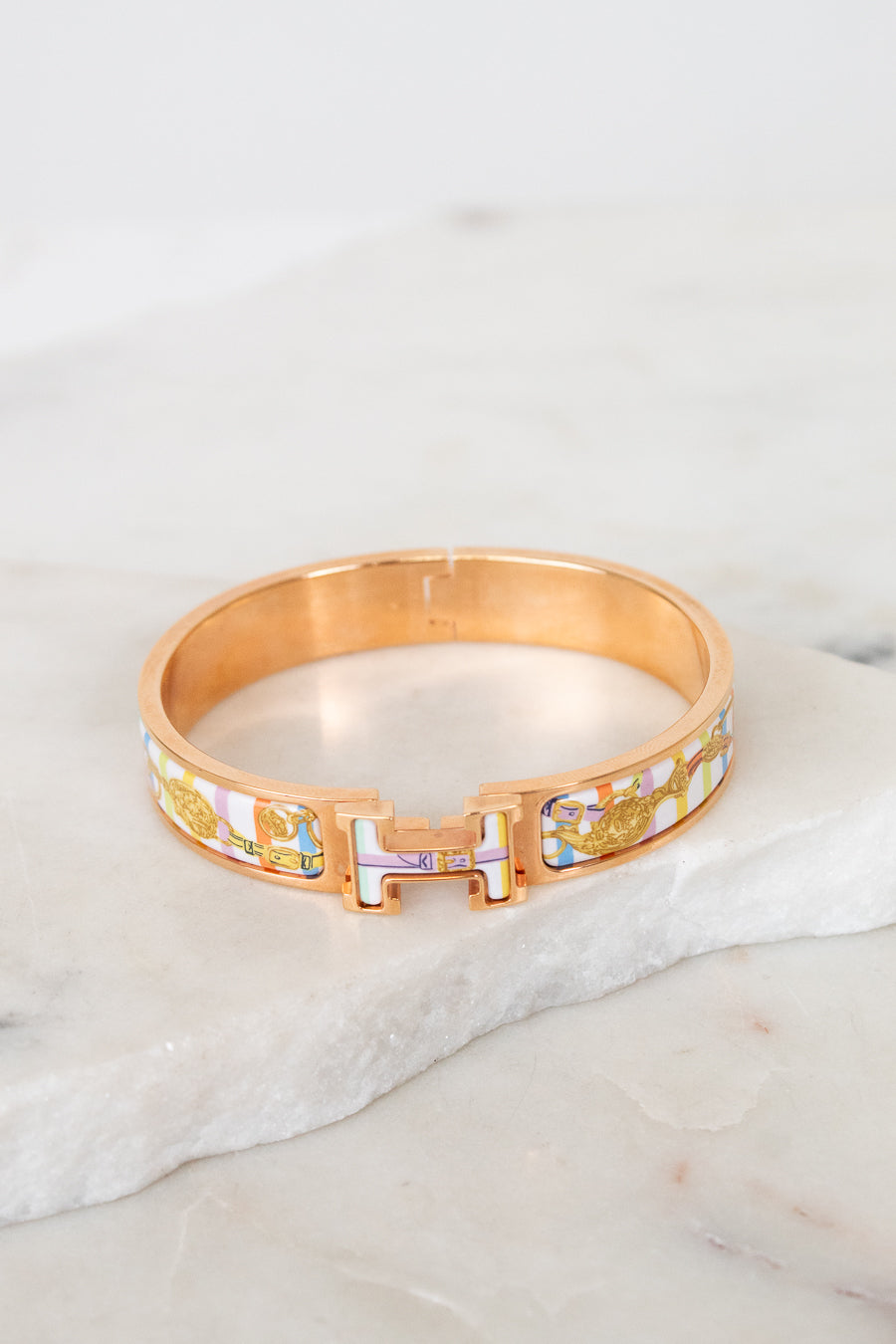 Rose gold bracelet with multicolor letters on a marble surface