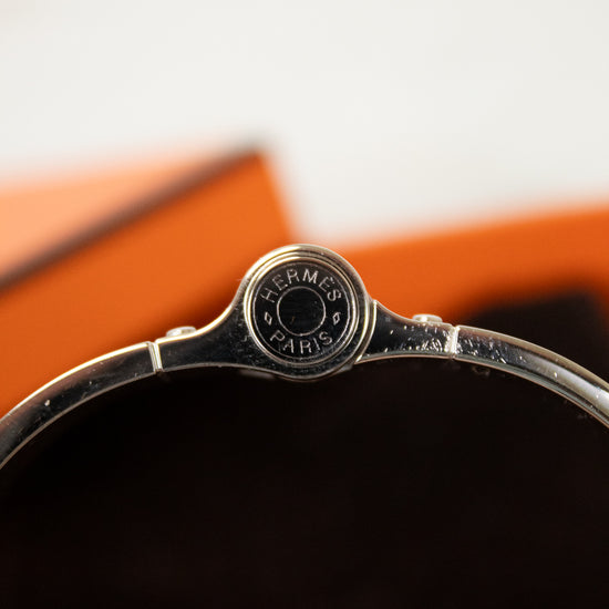Close-up of a silver Hermès bracelet with an orange background