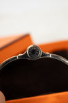 Close-up of a silver Hermès bracelet with an orange background