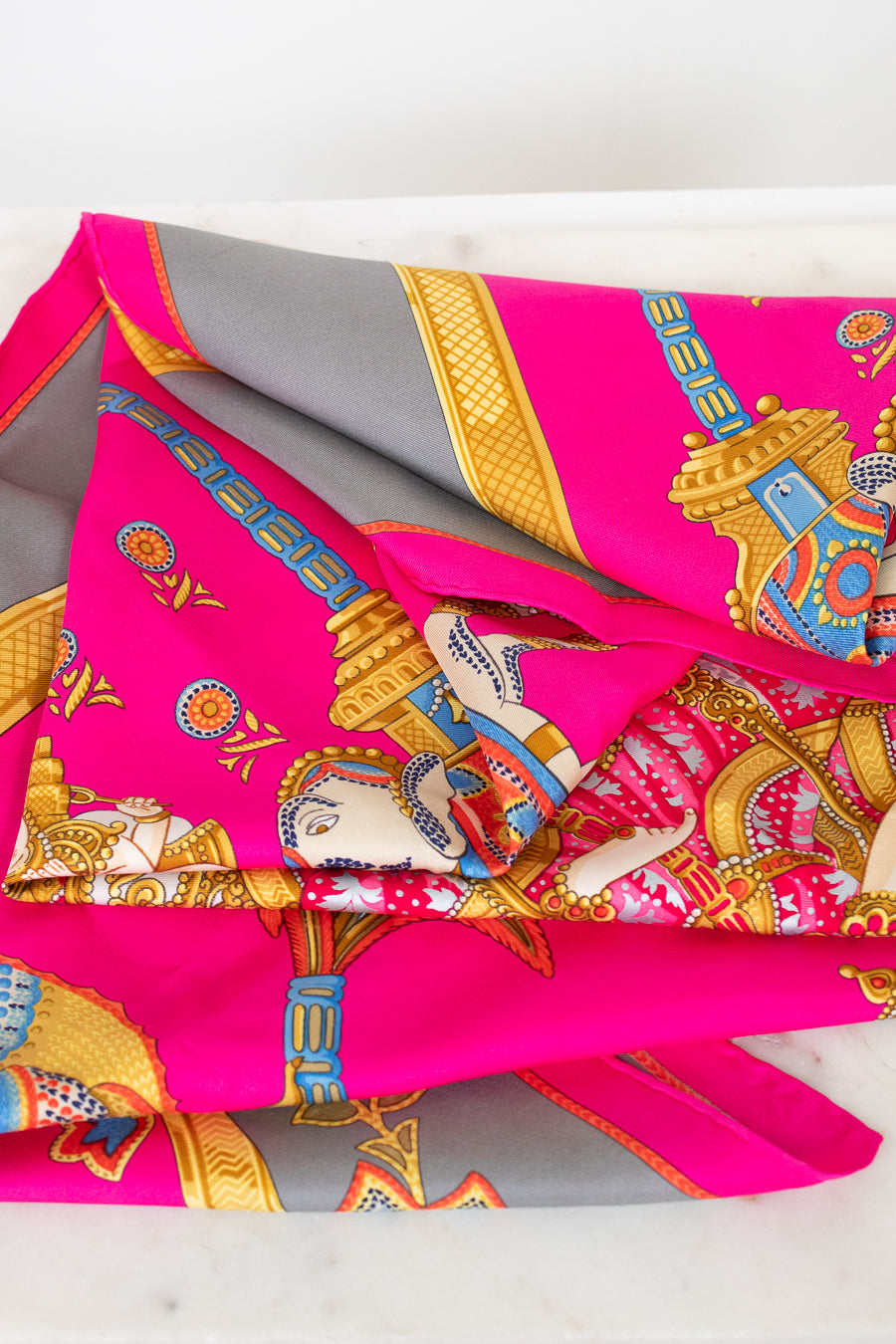 Colorful patterned fabric scarf with pink and gold design on a white background