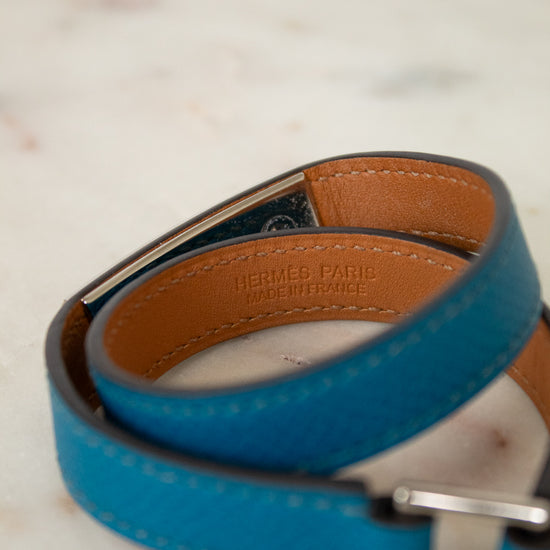 Blue leather bracelet with brown interior and silver buckle on a marble surface