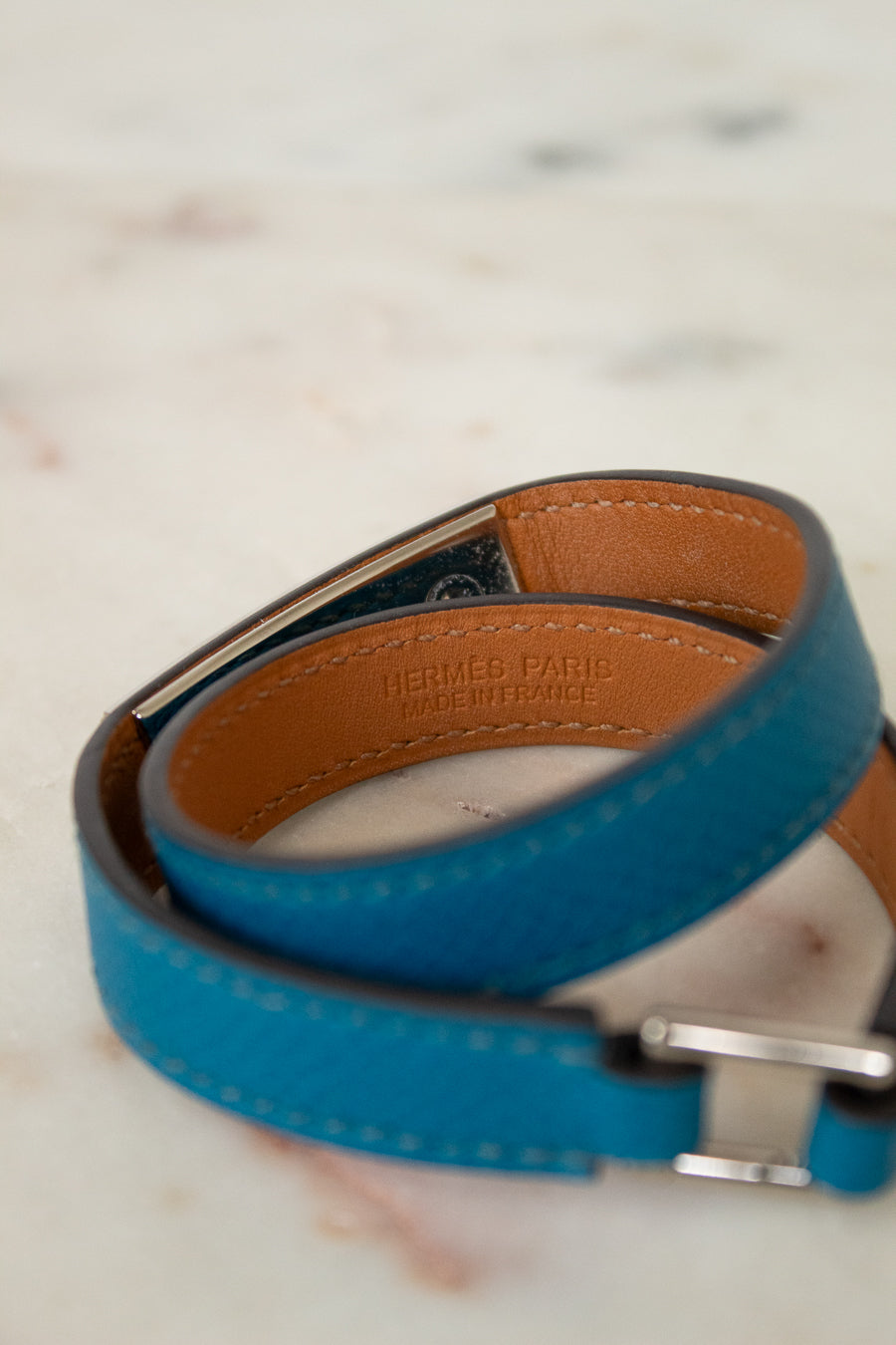 Blue leather bracelet with brown interior and silver buckle on a marble surface