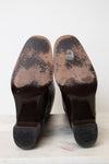 A pair of dark brown leather boots shown from the sole, revealing heavily worn and scuffed soles with visible scuffing and a white marking on the upper portions.
