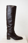 A side view of the HERMES black boot, showing the black heel and slouchy wrinkle. With a white background.