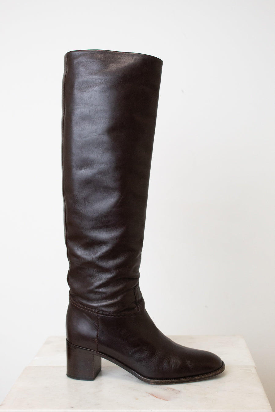 A side view of the HERMES black boot, showing the black heel and slouchy wrinkle. With a white background.