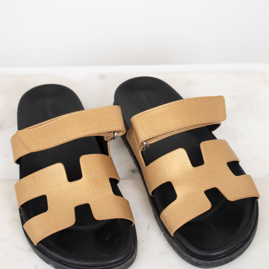 Pair of gold and black sandals on a white marble surface