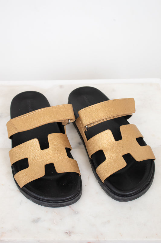 Pair of gold and black sandals on a white marble surface