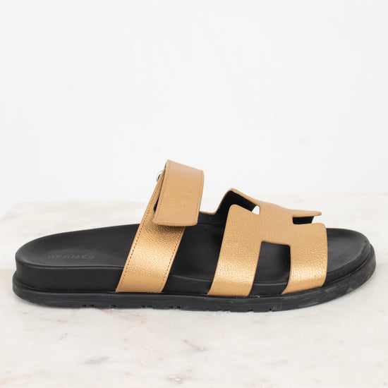 Black sandal with gold straps on a white marble background