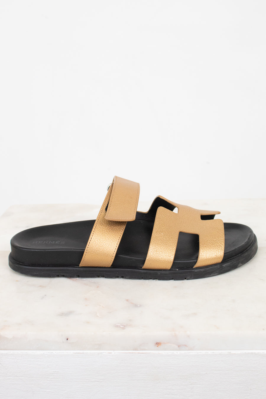 Black sandal with gold straps on a white marble background