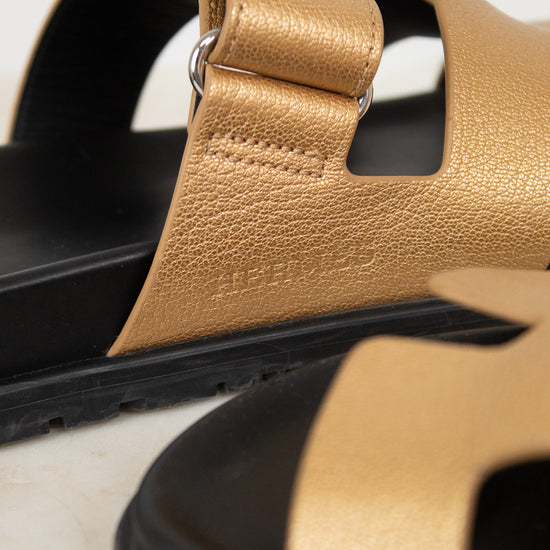 Close-up of Hermes logo on gold and black sandals