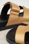 Close-up of Hermes logo on gold and black sandals