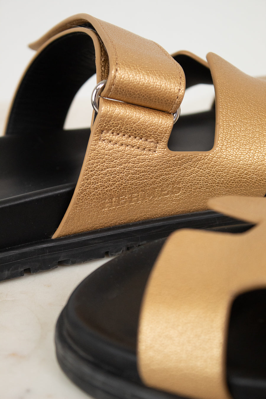 Close-up of Hermes logo on gold and black sandals