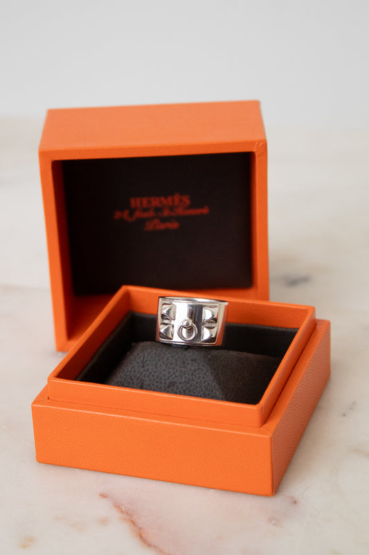 Silver HERMES ring with a geometric design and central circular detail, displayed in an orange HERMES jewelry box on a white background.