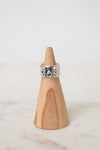 Silver HERMES ring with a wide band, geometric cutout details, and a central circular motif, displayed on a wooden ring stand.The ring is placed on a wooden ring stand with a white background.