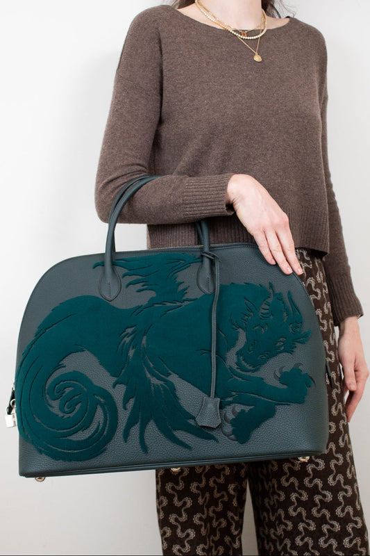 Person holding a teal handbag with a dragon design against a white background