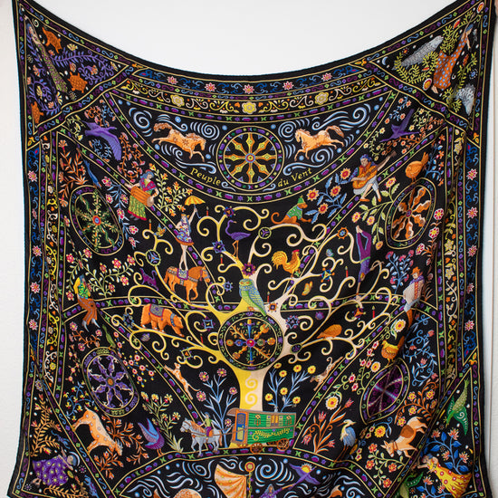  a black silk scarf with a vibrant, multicolored bohemian print featuring peacocks, flowers, and traditional patterns against a white background