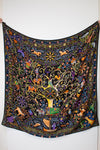  a black silk scarf with a vibrant, multicolored bohemian print featuring peacocks, flowers, and traditional patterns against a white background