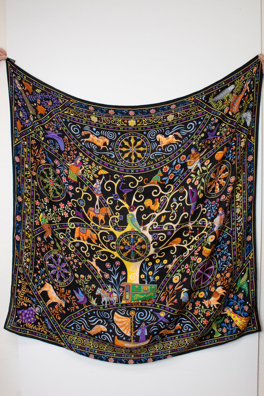  a black silk scarf with a vibrant, multicolored bohemian print featuring peacocks, flowers, and traditional patterns against a white background