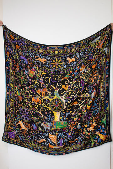  a black silk scarf with a vibrant, multicolored bohemian print featuring peacocks, flowers, and traditional patterns against a white background