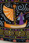 A close-up of a black textile scarf featuring a highly detailed, colorful folk-art print with horses, parrots, a rooster, floral motifs, and swirling gold lines. The text 'Hermes-Paris' printed across the center.
