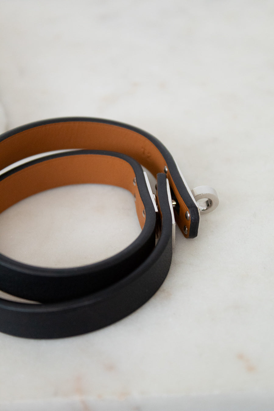 Two leather belts, one black and one brown, on a marble surface.