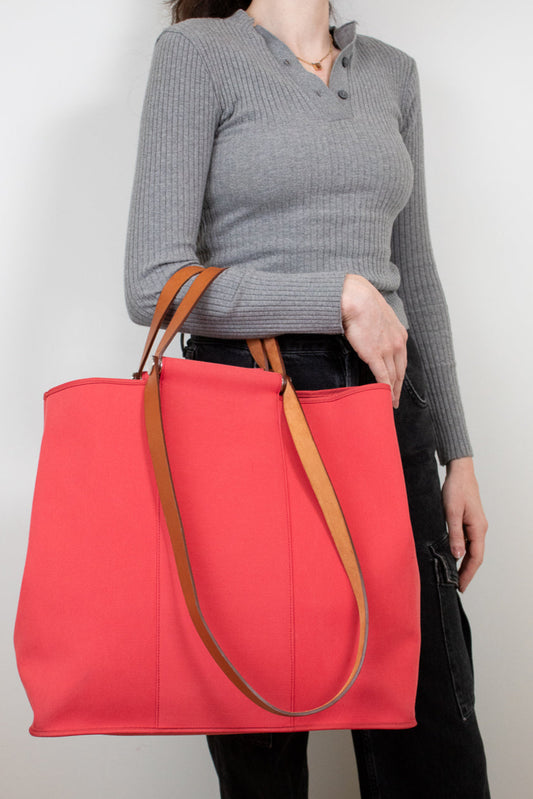 Person holding large red canvas tote bag with brown leather straps on white background