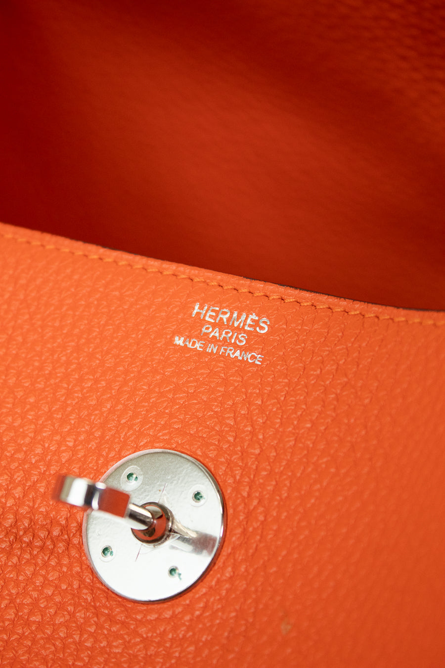 Close-up of an orange textured leather bag interior with silver-tone hardware and visible HERMES PARIS MADE IN FRANCE branding stitched into the leather.