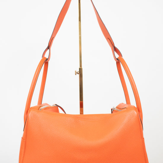 An orange pebbled leather shoulder bag with a gold-tone metal stand, photographed against a plain white background.