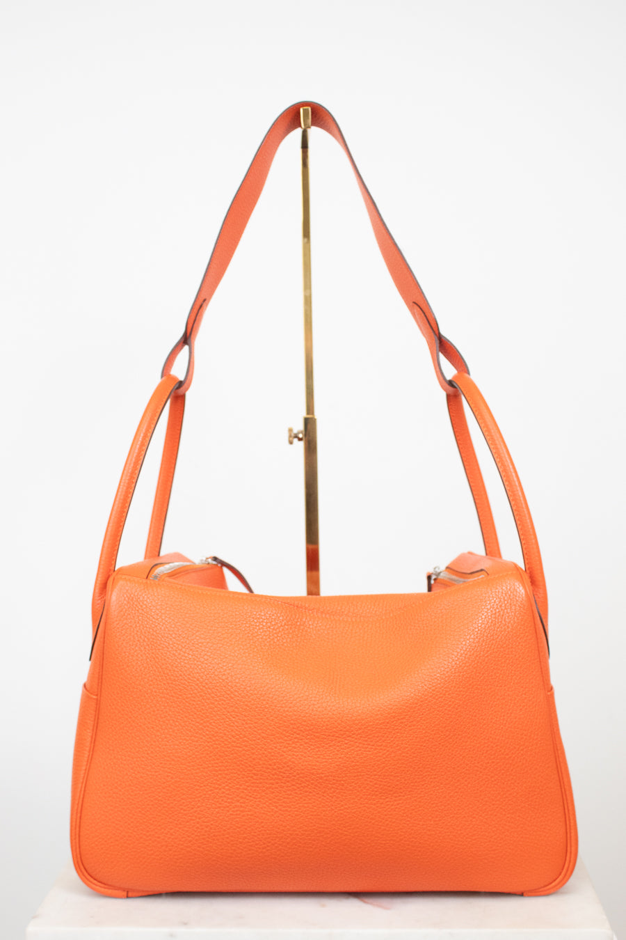 An orange pebbled leather shoulder bag with a gold-tone metal stand, photographed against a plain white background.