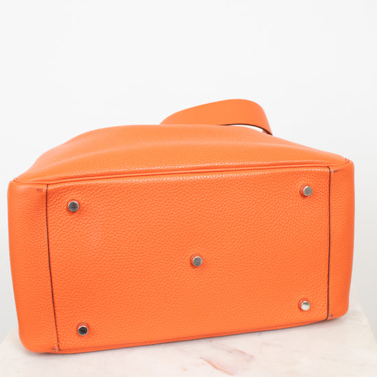Bright orange pebbled leather handbag shown from the bottom, featuring silver-tone metal studs and a matching orange strap, set against a plain white background.