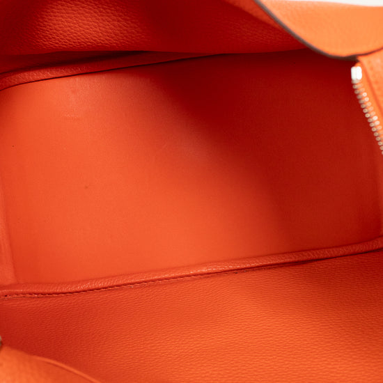Close-up of the interior of a bright orange pebbled leather bag, showing the lining, a zip pocket, and a metal snap closure.