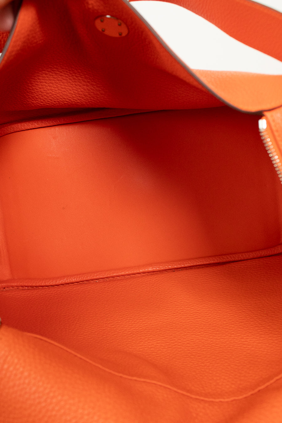 Close-up of the interior of a bright orange pebbled leather bag, showing the lining, a zip pocket, and a metal snap closure.