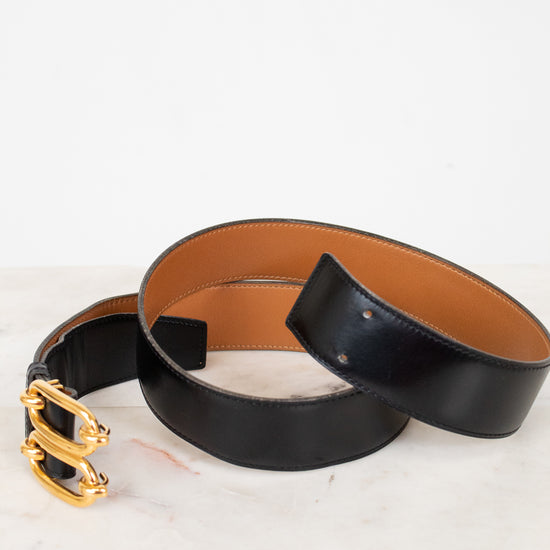 Black leather belt with gold buckle on a white marble surface