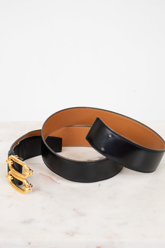 Black leather belt with gold buckle on a white marble surface