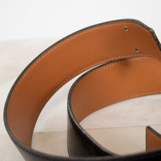 Close-up of a black leather belt with a brown interior on a light background