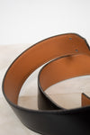 Close-up of a black leather belt with a brown interior on a light background