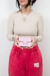 Person holding a pink handbag wearing a beige sweater and red pants with 'wang' branding.