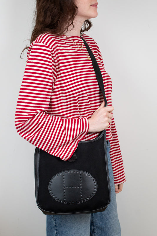 Person wearing a red and white striped shirt holding a black bag with a visible "H" brand logo.