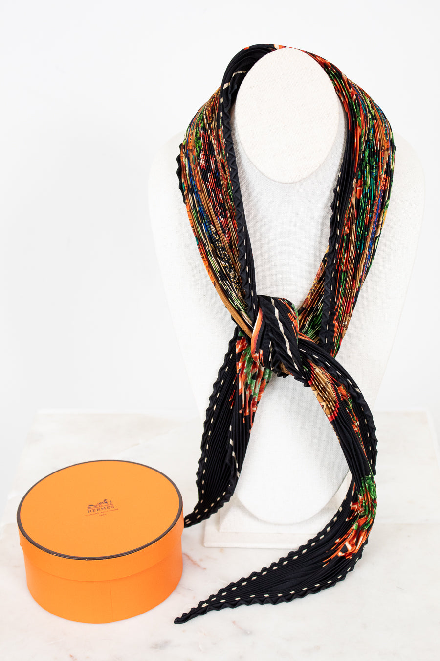 Colorful patterned scarf on a necklace best with an orange box below on a white background