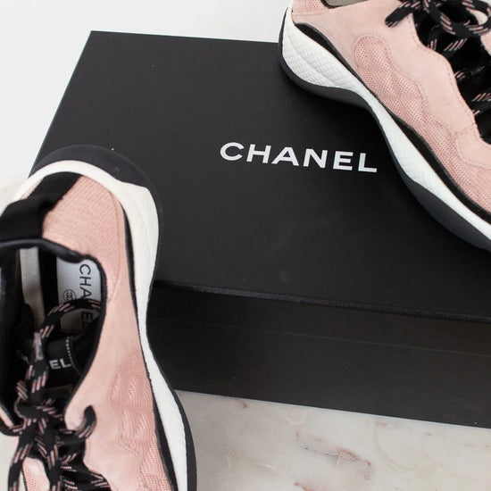 Pink and black Chanel sneakers on a Chanel box with a white background