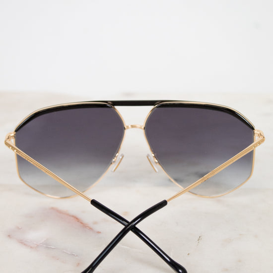 Gold-framed sunglasses with dark gradient lenses on a marble surface