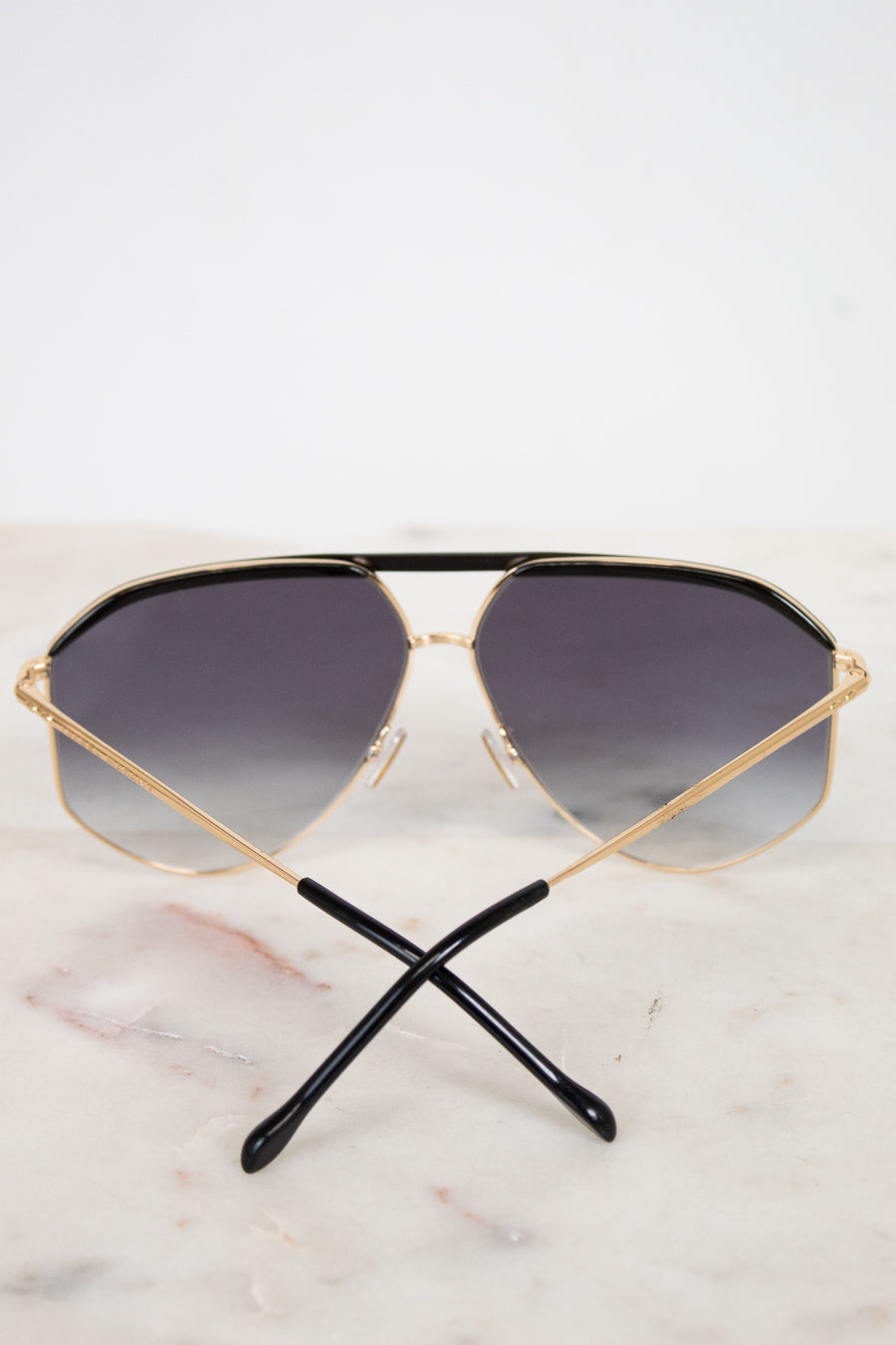 Gold-framed sunglasses with dark gradient lenses on a marble surface