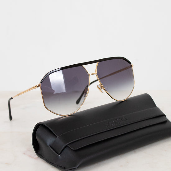 Sunglasses with gold frame and gradient lenses on a white surface with black case.