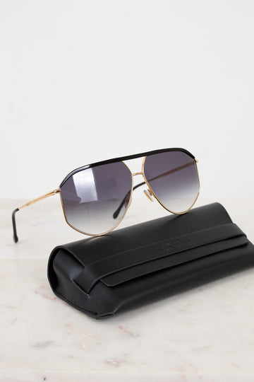 Sunglasses with gold frame and gradient lenses on a white surface with black case.